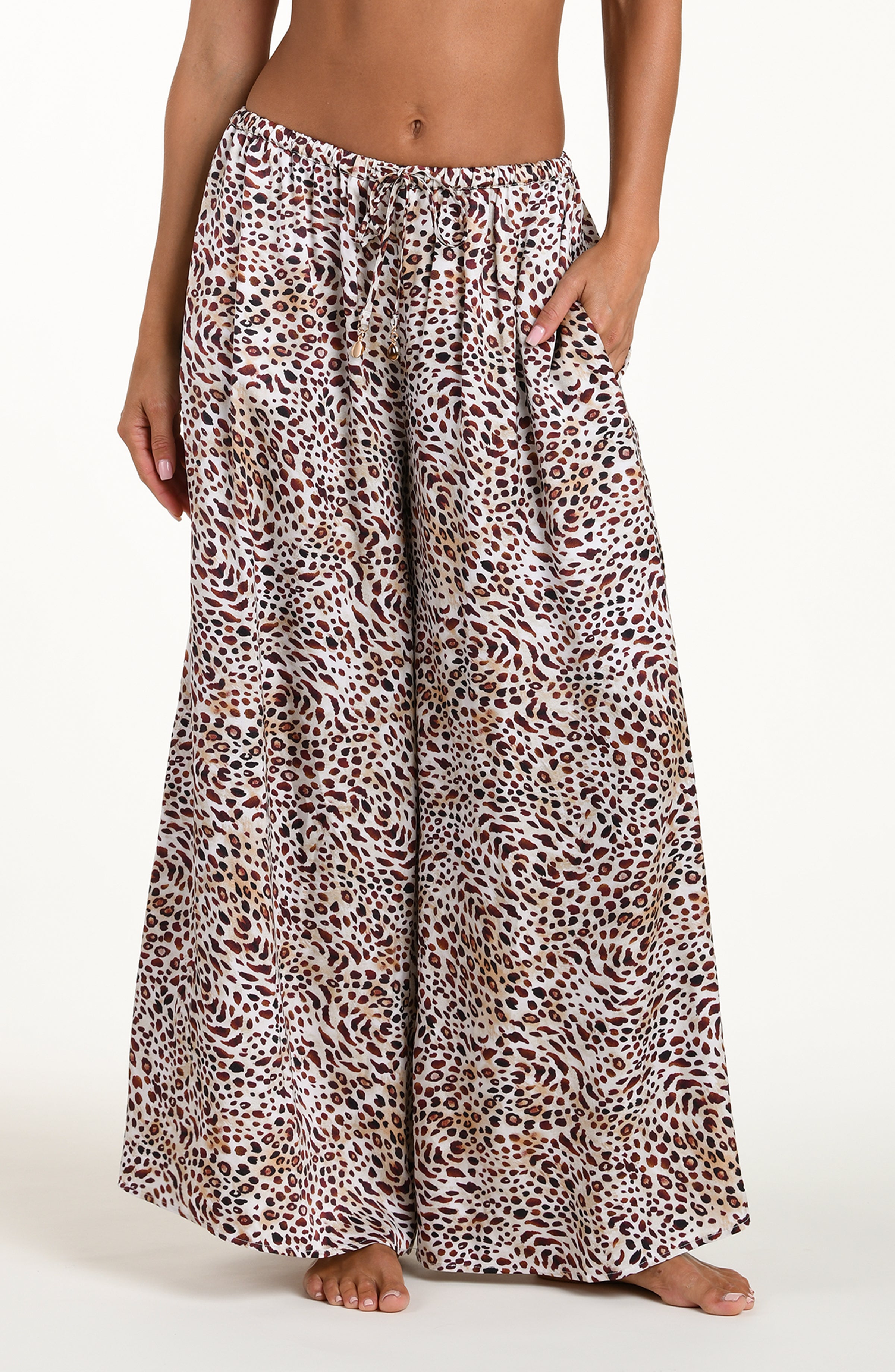 Front image of model wearing leopard printed beach pants with an elastic waist and pockets. 