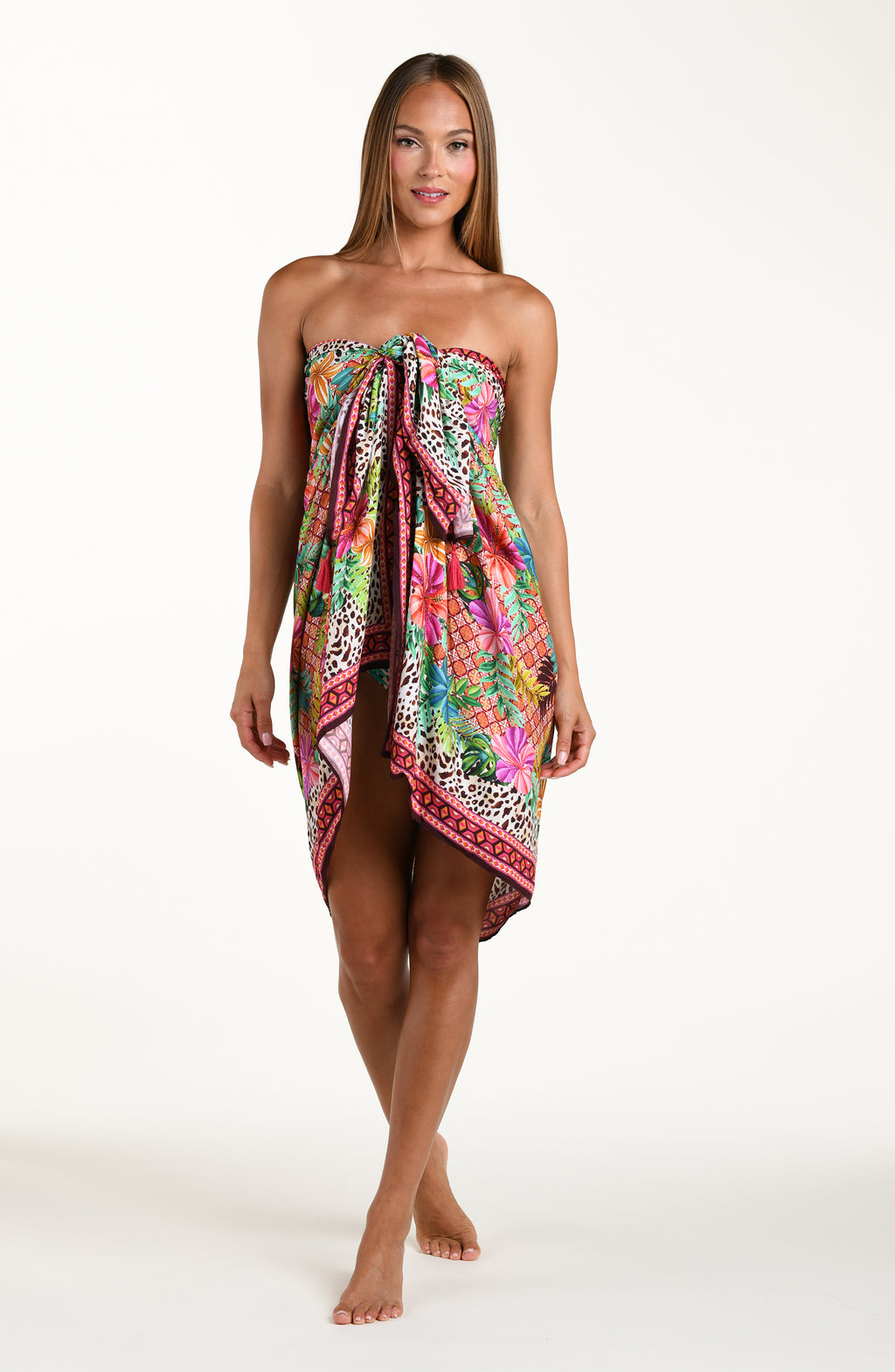 Full body front image of model wearing a multicolored tropical and leopard printed pareo wrap featuring a tie side. Model is showcasing the pareo wrapped above the bust. 