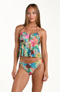 Front image of model wearing a multicolored tropical printed midkini top featuring adjustable halter straps, keyhole, and flounce detail. This is paired with a matching bikini bottom.