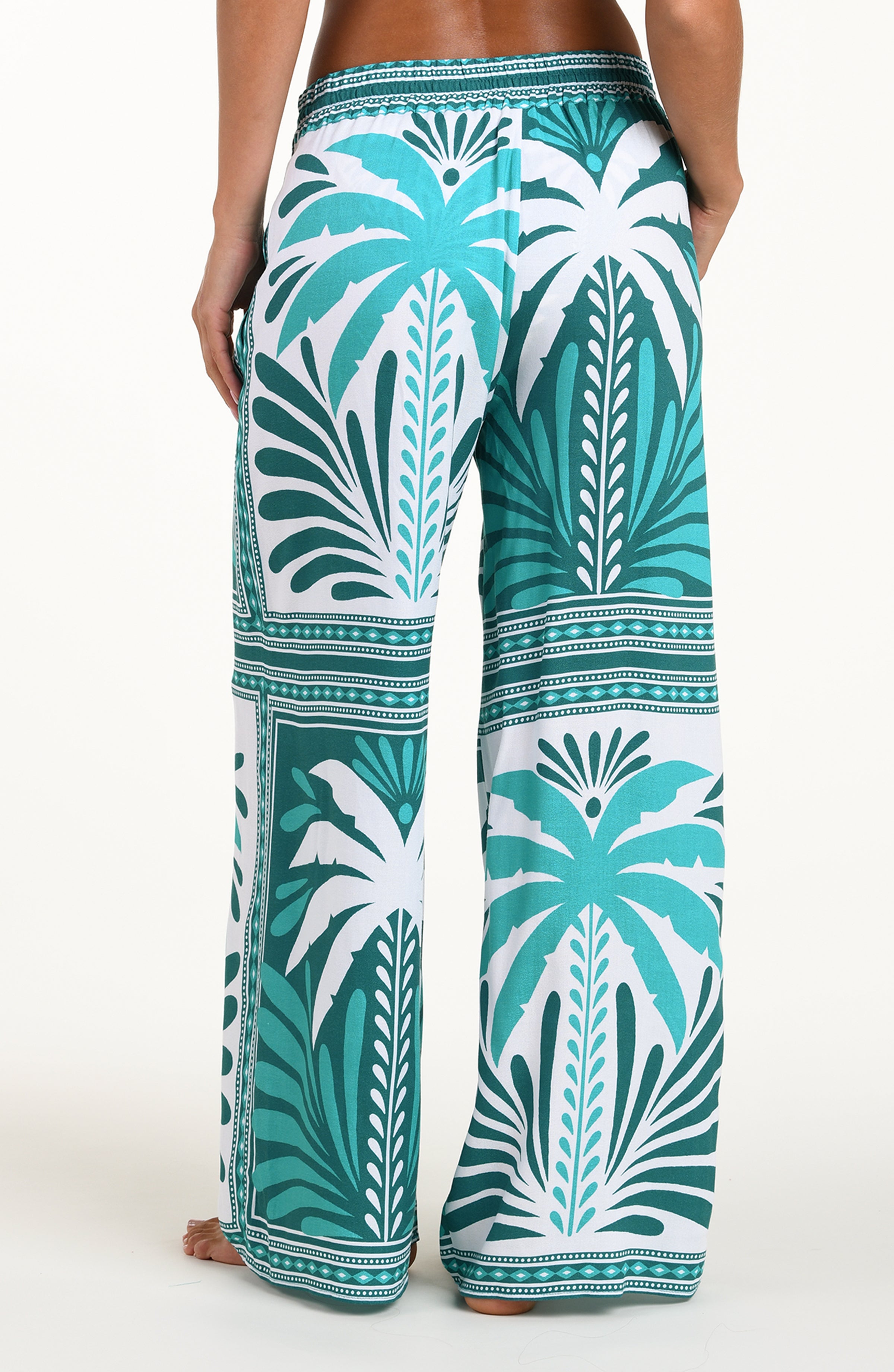Pants with a palm tree pattern in teal and white on a white background