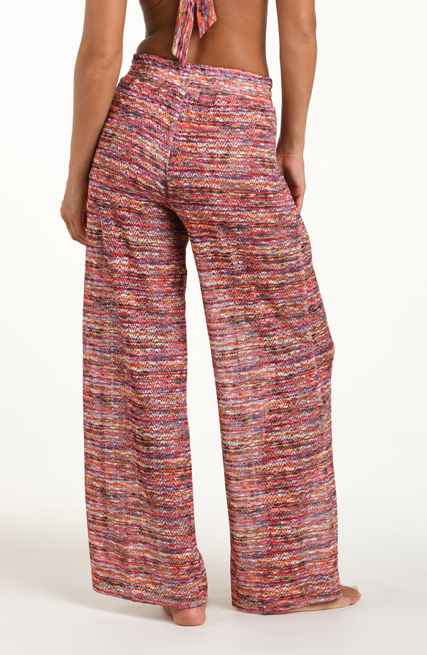 Back image of model wearing long beach pants in a multicolored ripple pattern featuring an elastic waist. 