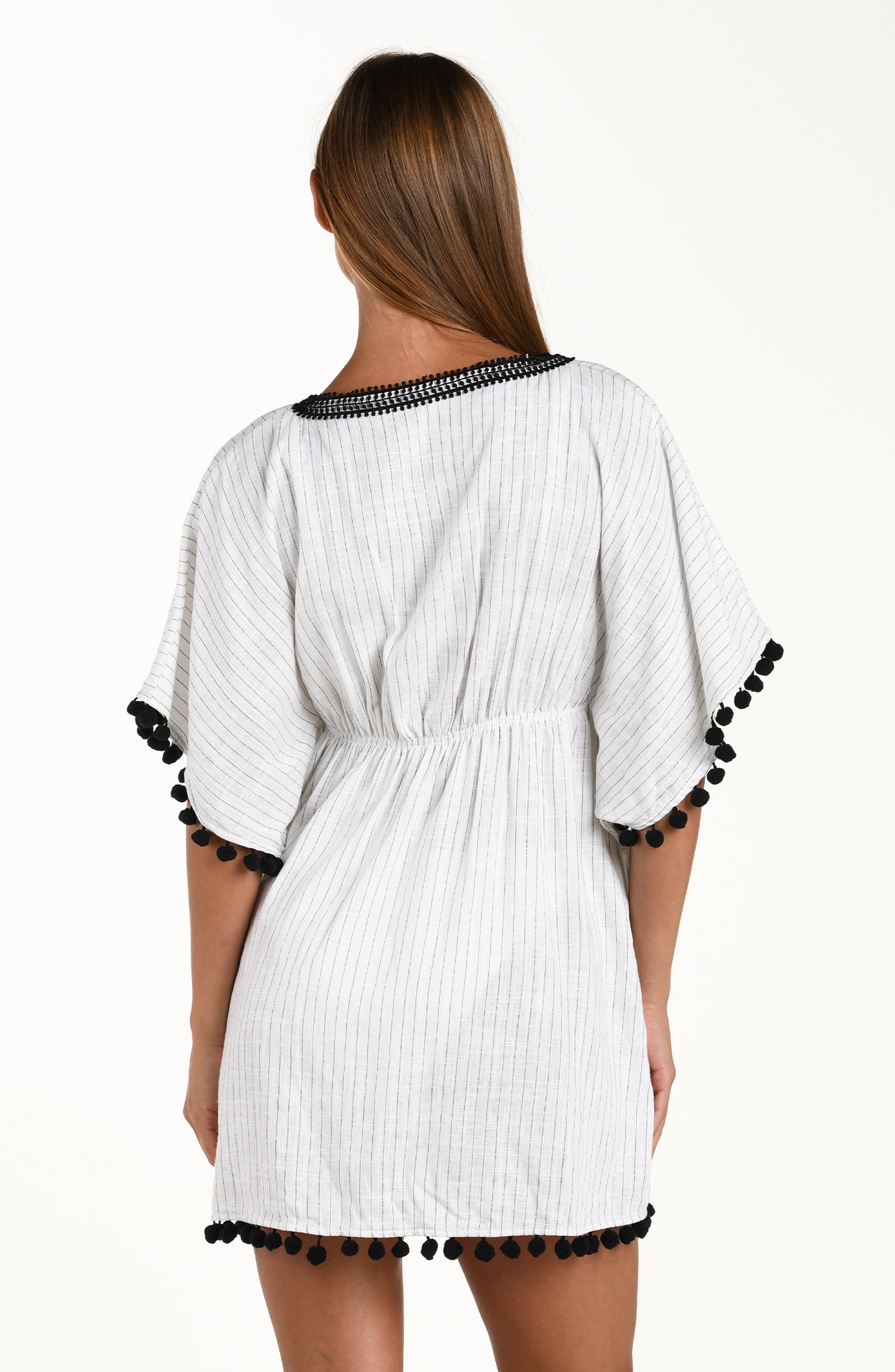 
                  
                    Back image of model wearing a short pull over v-neck caftan with three quarter sleeves adorned with tassel trim. Featuring a cream colored linen print.
                  
                