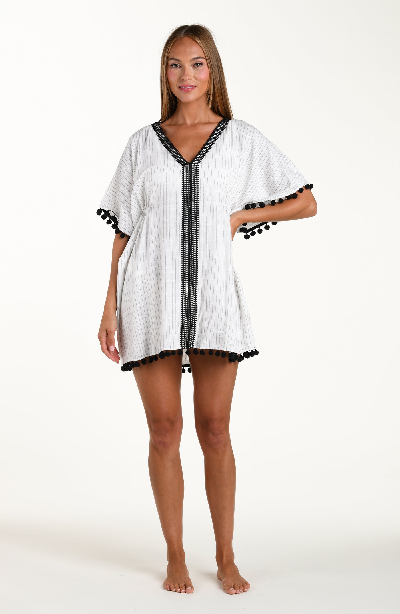 
                  
                    Full body front image of model wearing a short pull over v-neck caftan with three quarter sleeves adorned with tassel trim. Featuring a cream colored linen print.
                  
                