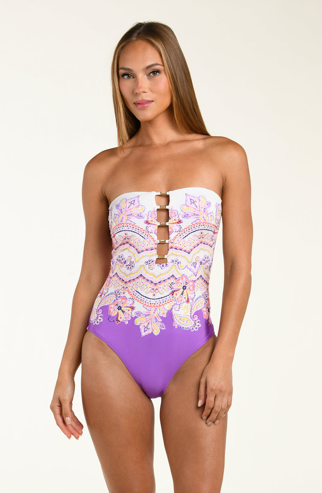 Woman wearing a purple multicolored floral one piece swimsuit against a white background.