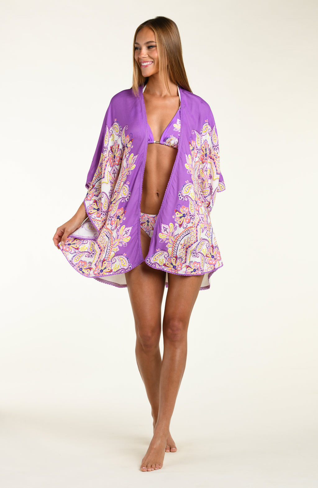 Woman wearing a purple multicolored floral kimono cover up over a white background