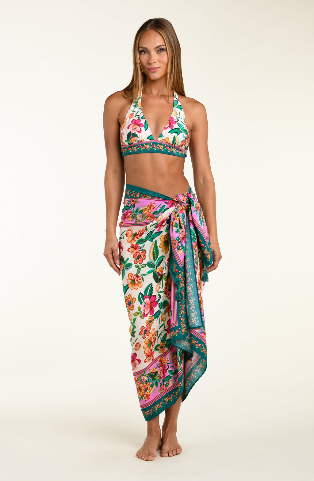 Woman wearing a floral patterned bikini top and matching pareo cover up worn by a person on a white background