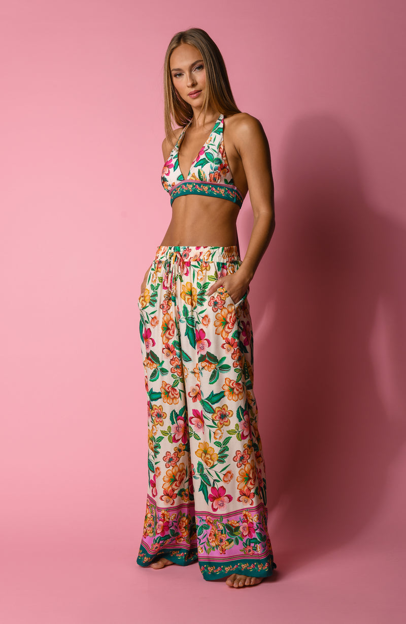Multicolored floral-patterned bikini top and matching beach pants worn by a person on a pink background
