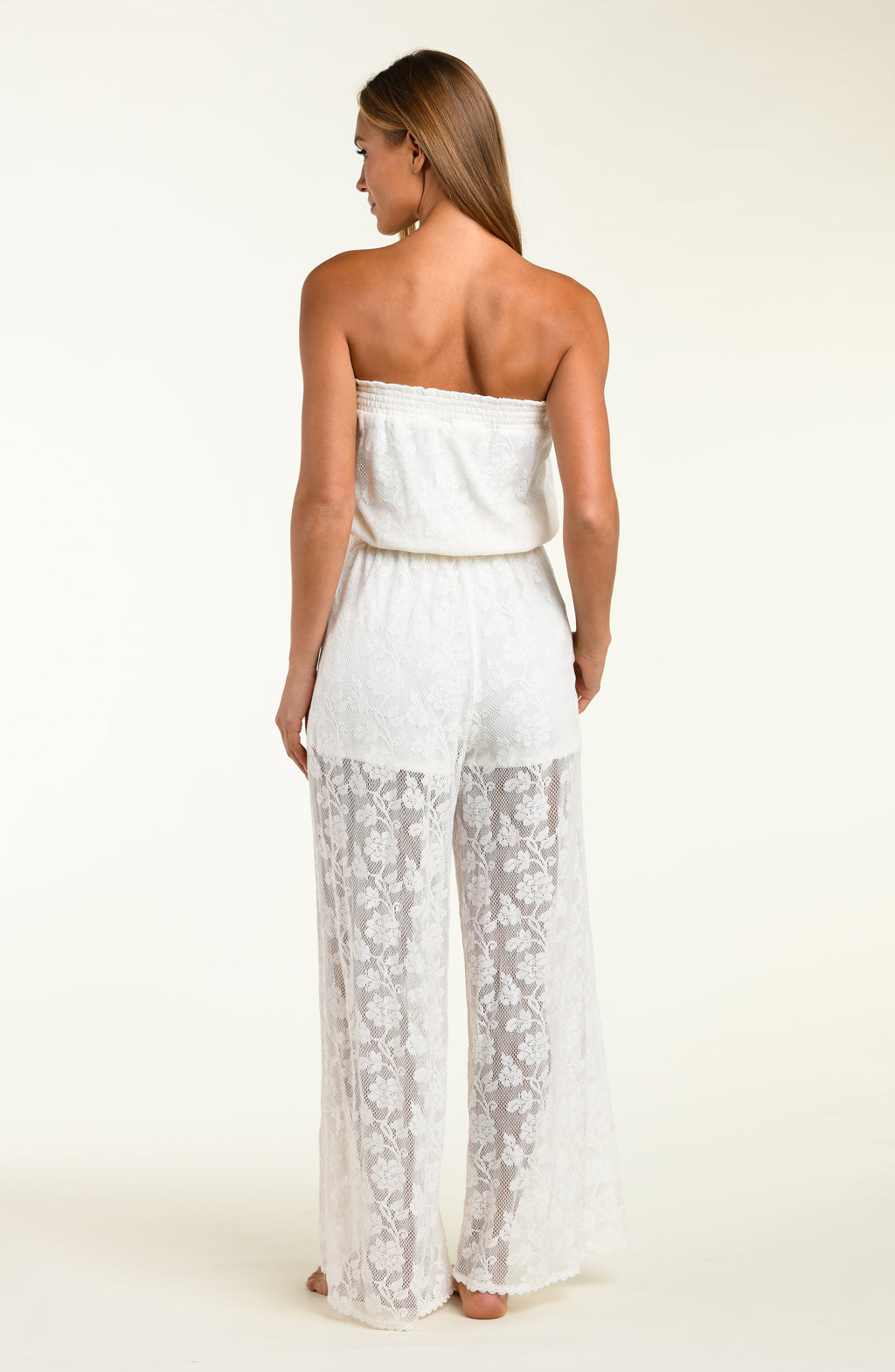 Woman wearing a white lace jumpsuit cover up against a white background.