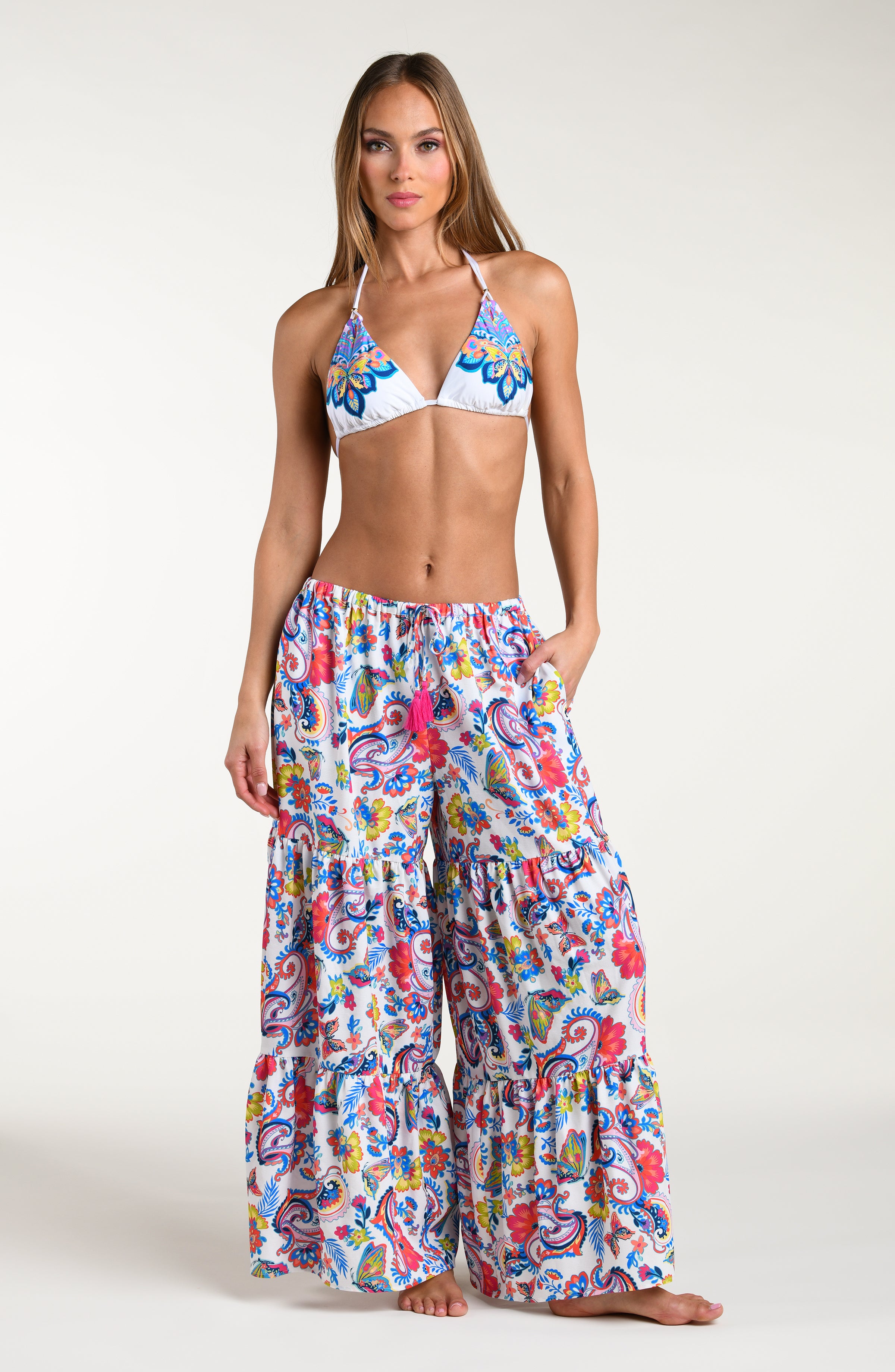 Woman wearing a multicolored bikini top and matching beach pants against a white background. 