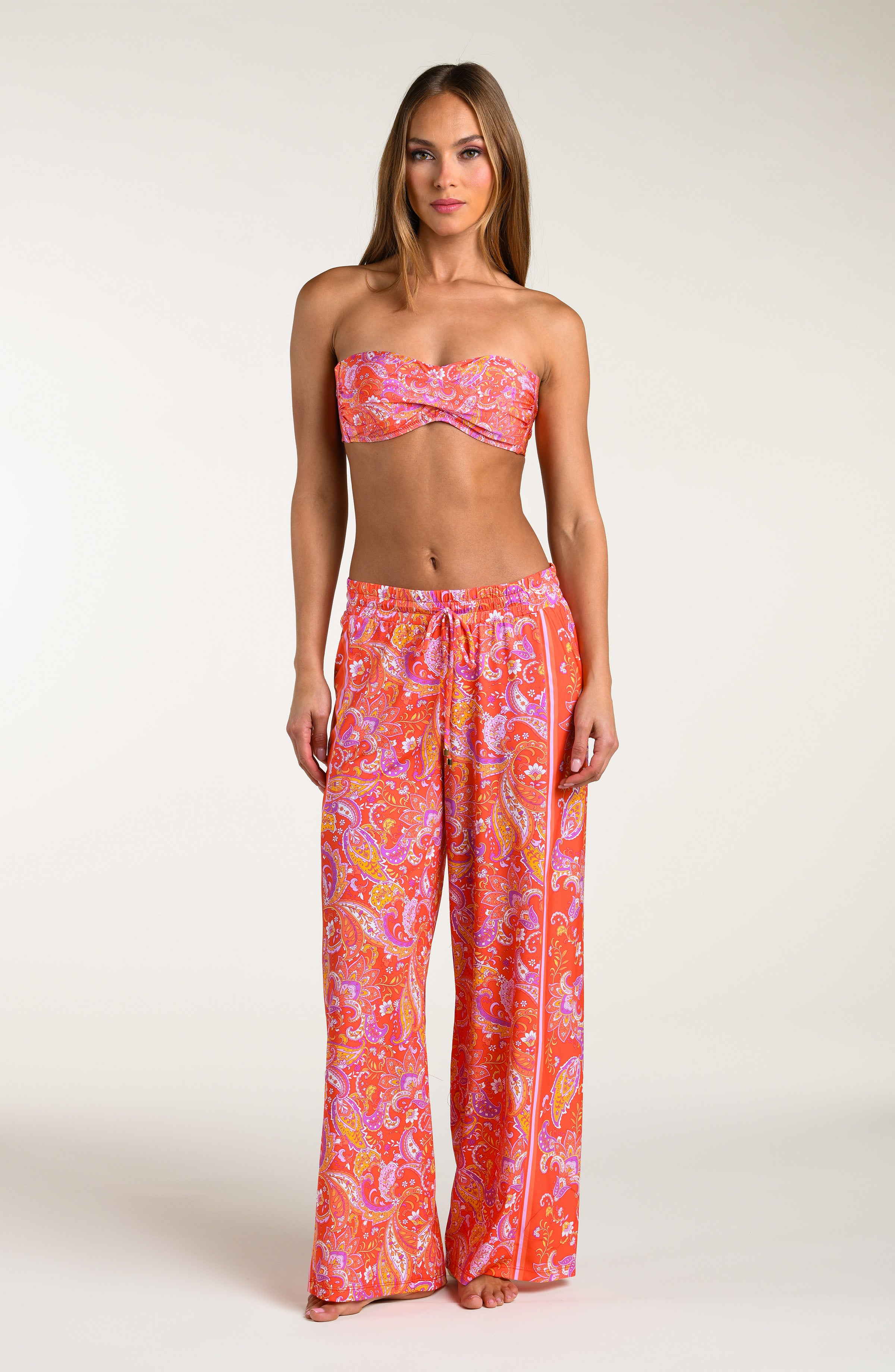 Woman wearing a pink and orange multicolored patterned bikini top and   matching pants worn by a person on a white background.