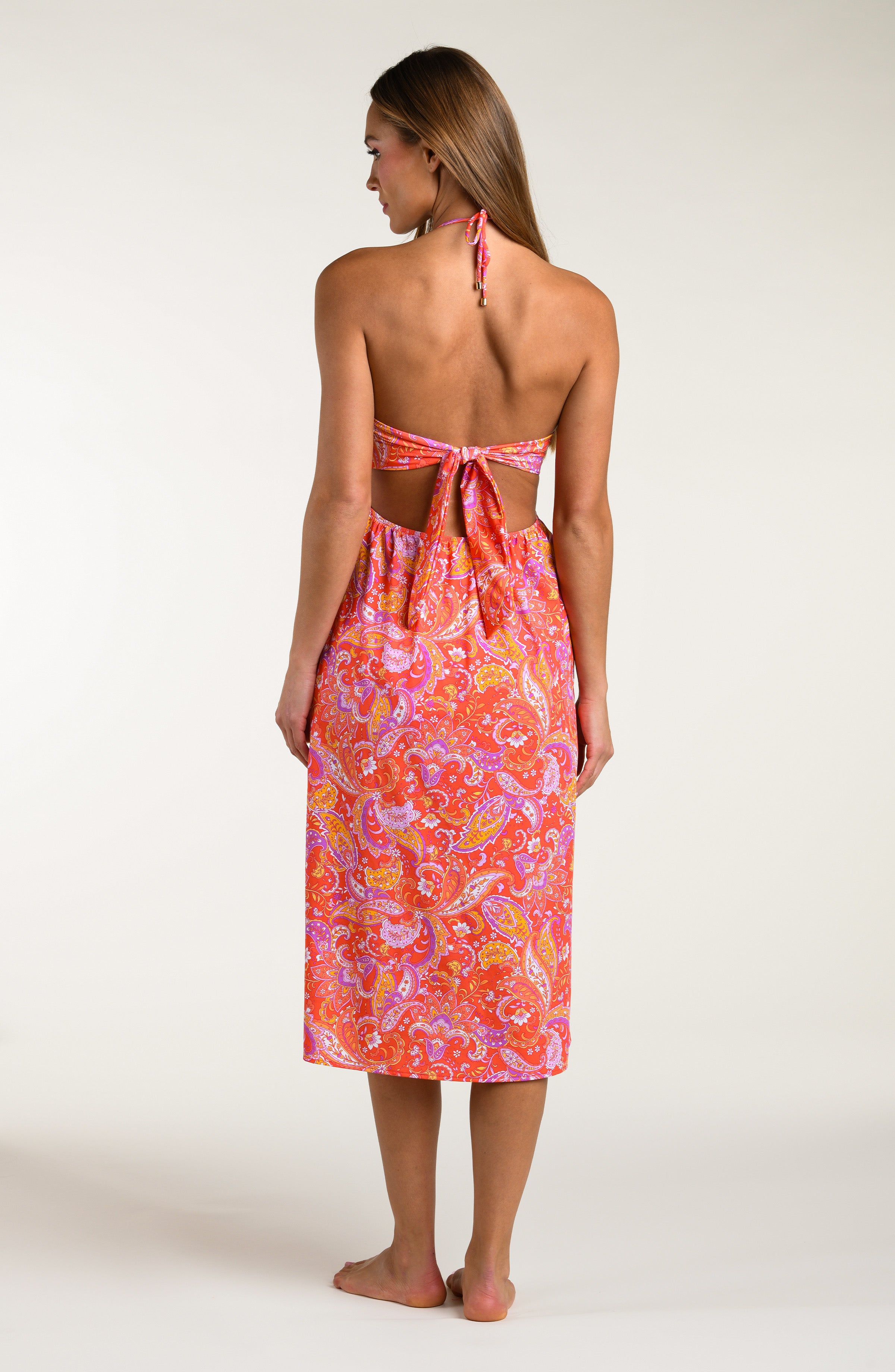 Woman wearing a pink and orange multicolored midi dress cover up against a white background.