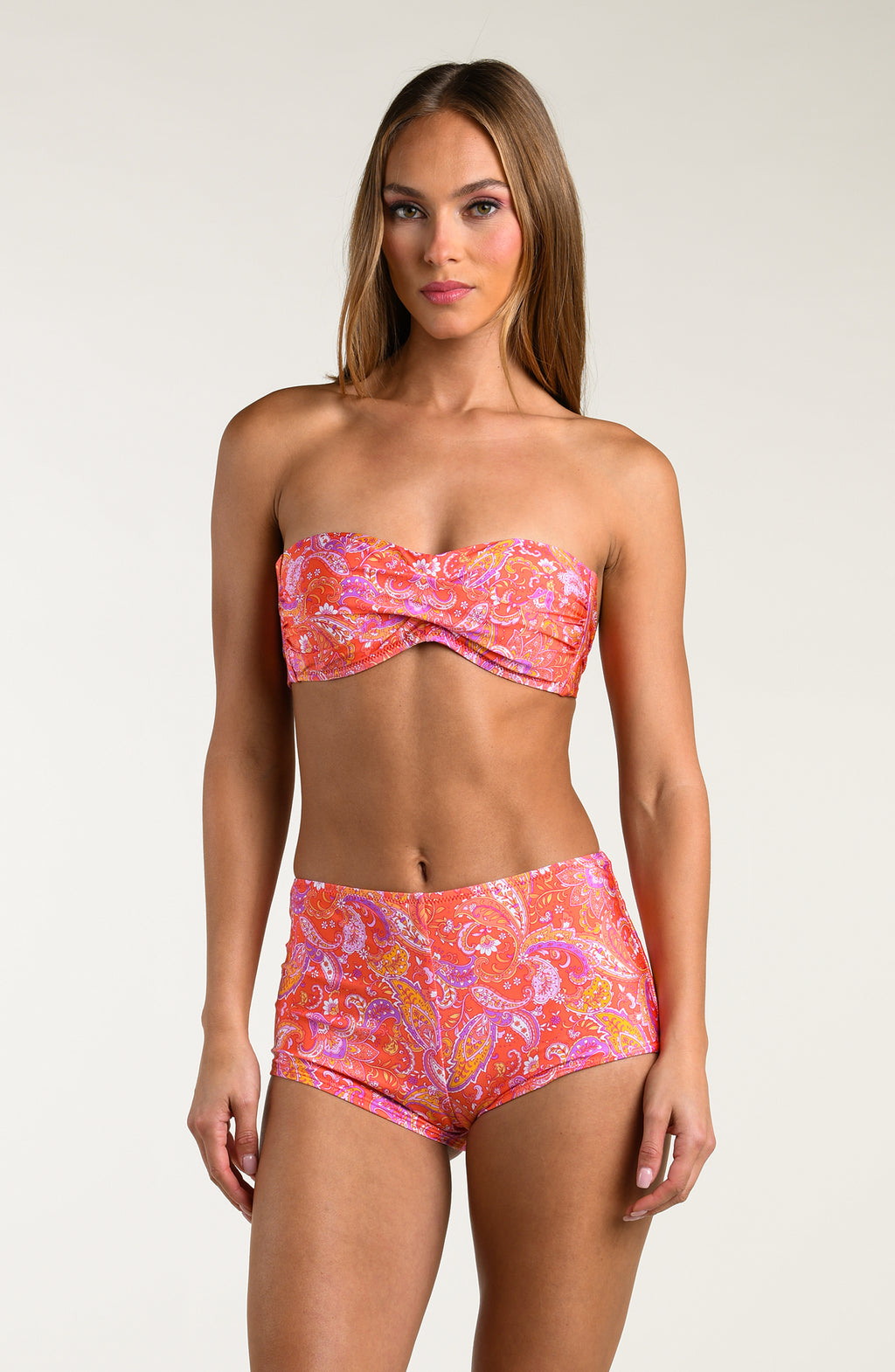 Woman wearing pink and orange multicolored bikini top and matching swim shorts on a white background