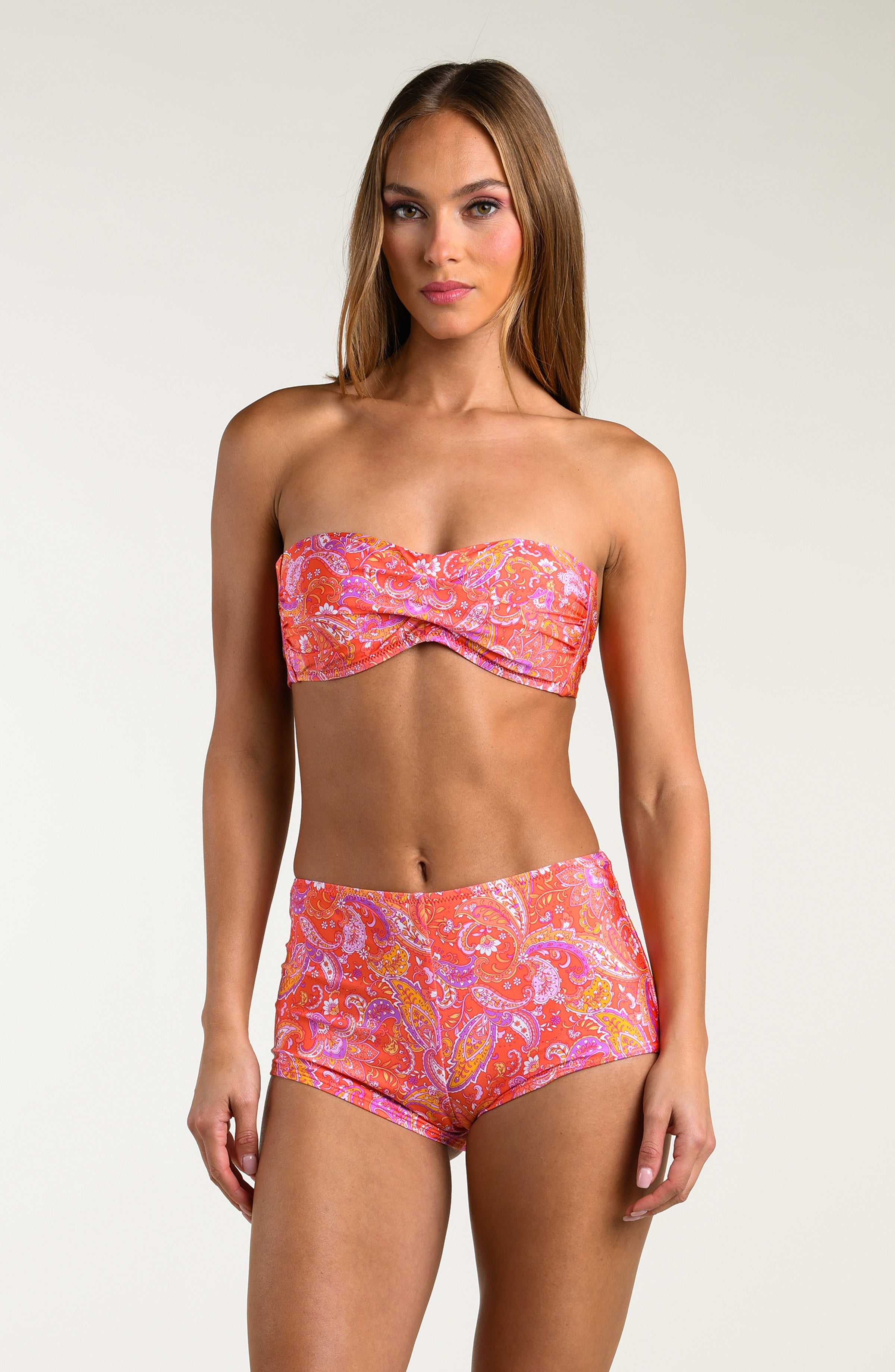 Woman wearing pink and orange multicolored bikini top and matching swim shorts on a white background