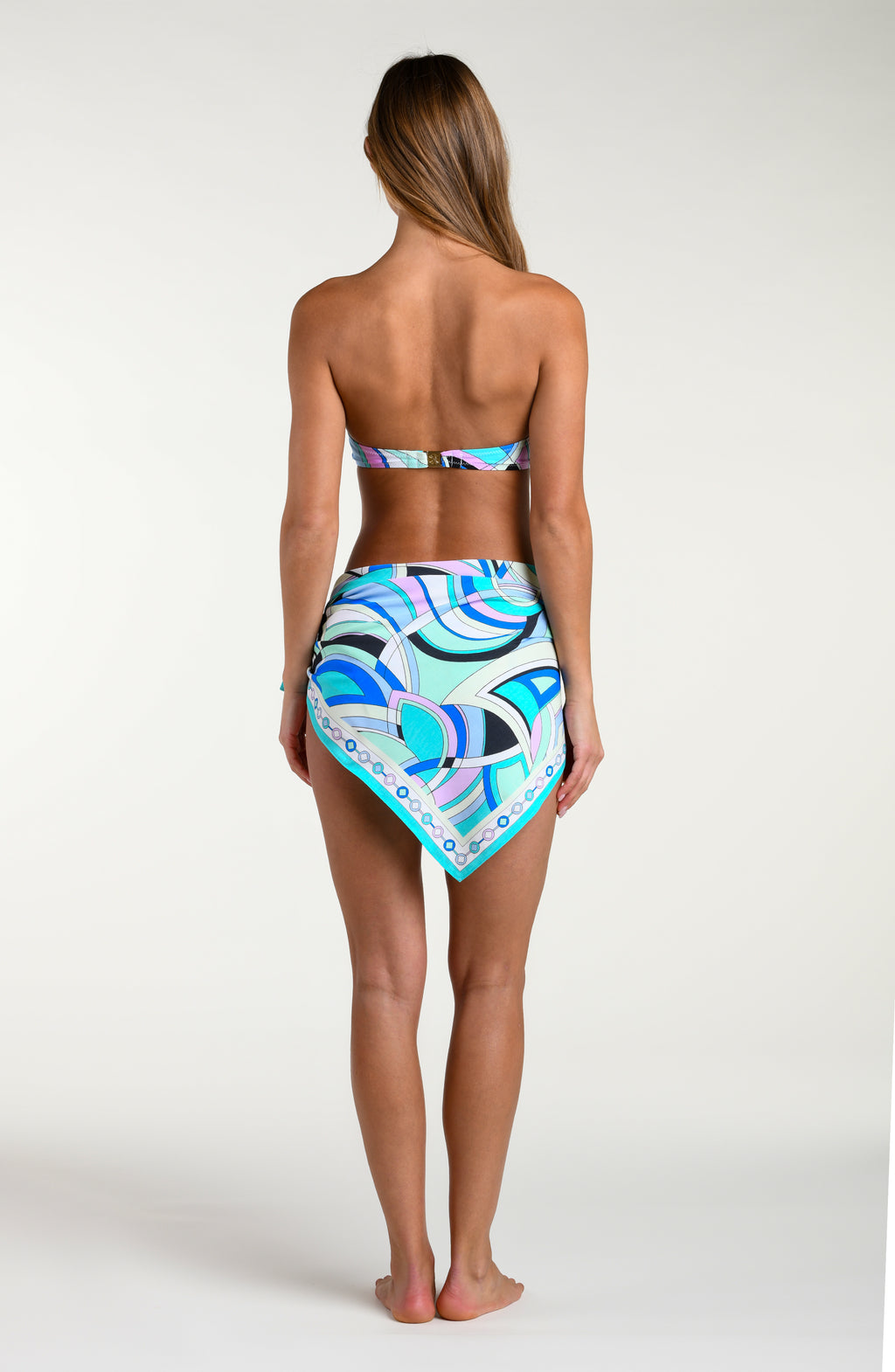 Woman wearing a multicolored bikini top and matching sarong against a white background. 