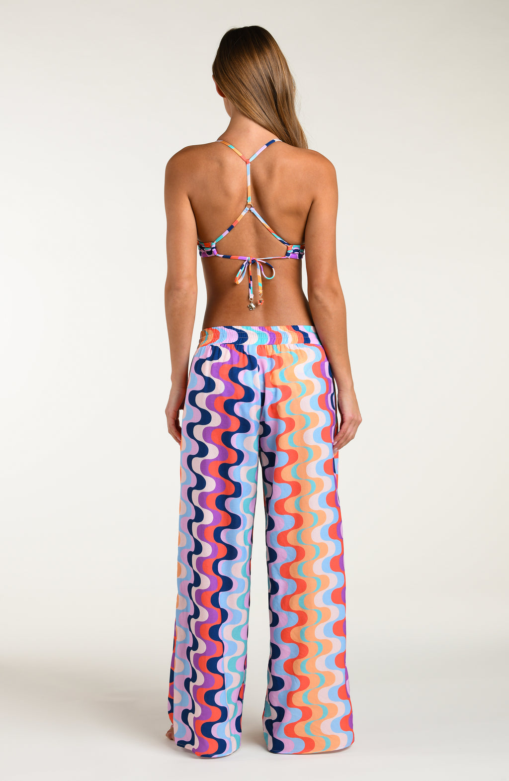 Woman wearing a colorful patterned bikini top and matching pants against a white background.