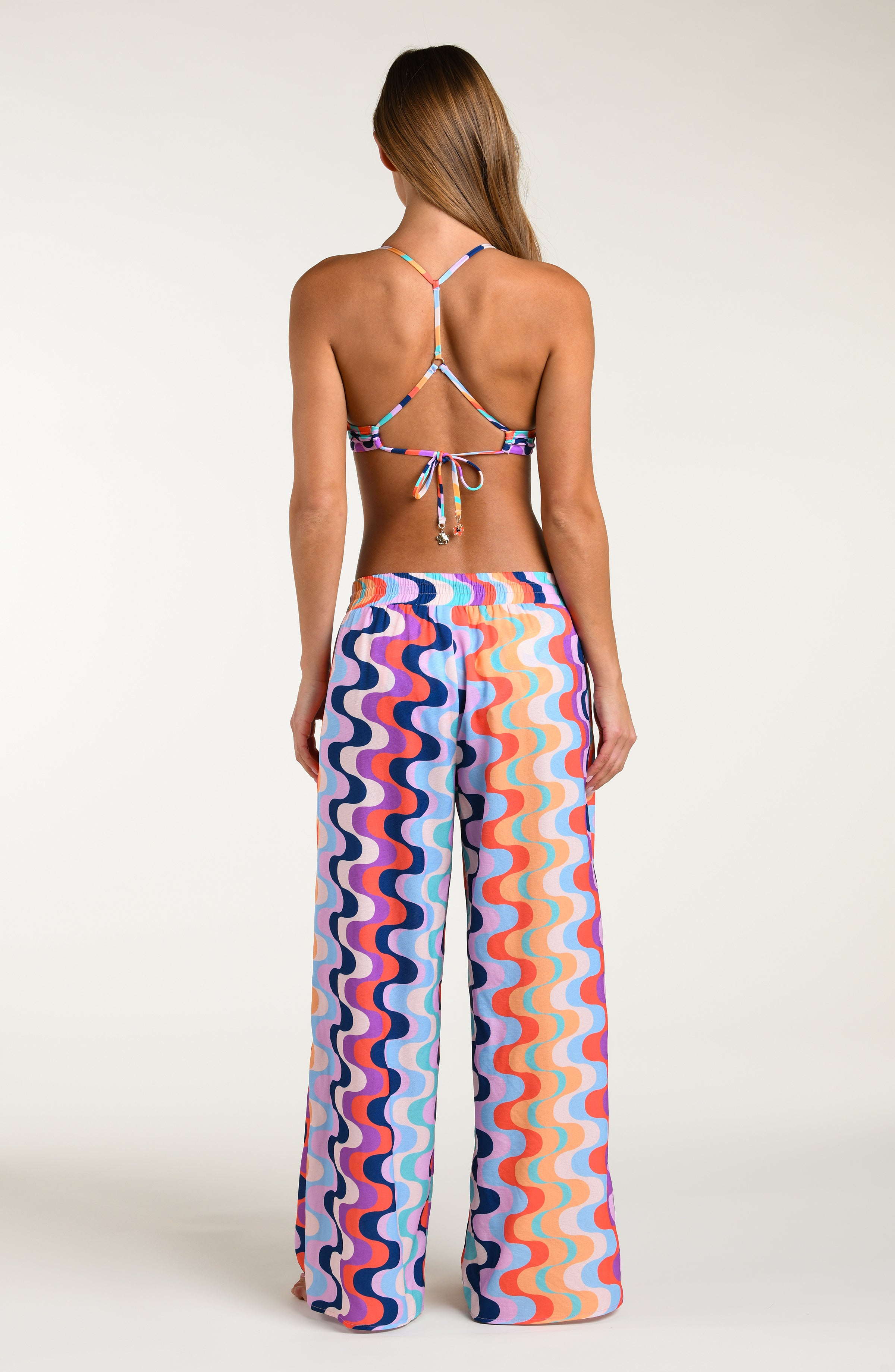 Woman wearing a colorful patterned bikini top and matching pants against a white background.