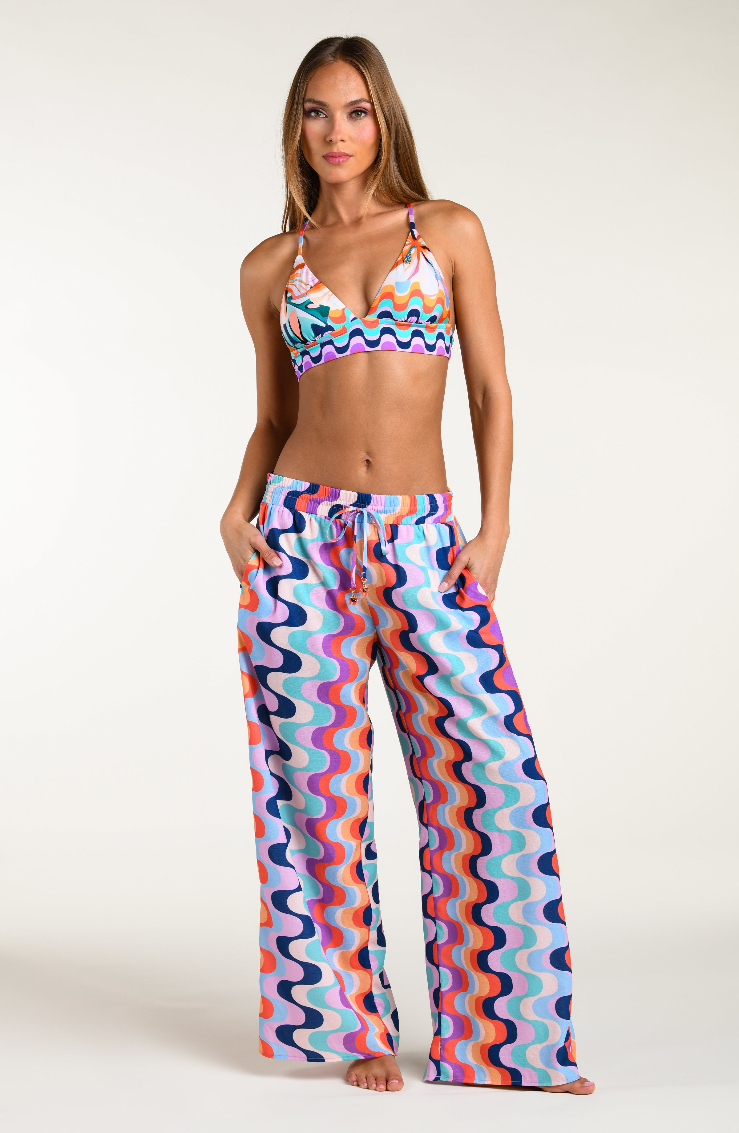 Woman wearing a colorful patterned bikini top and matching pants against a white background.