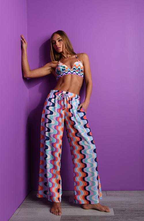 Woman wearing a multicolored bikini top and matching pants against a purple wall