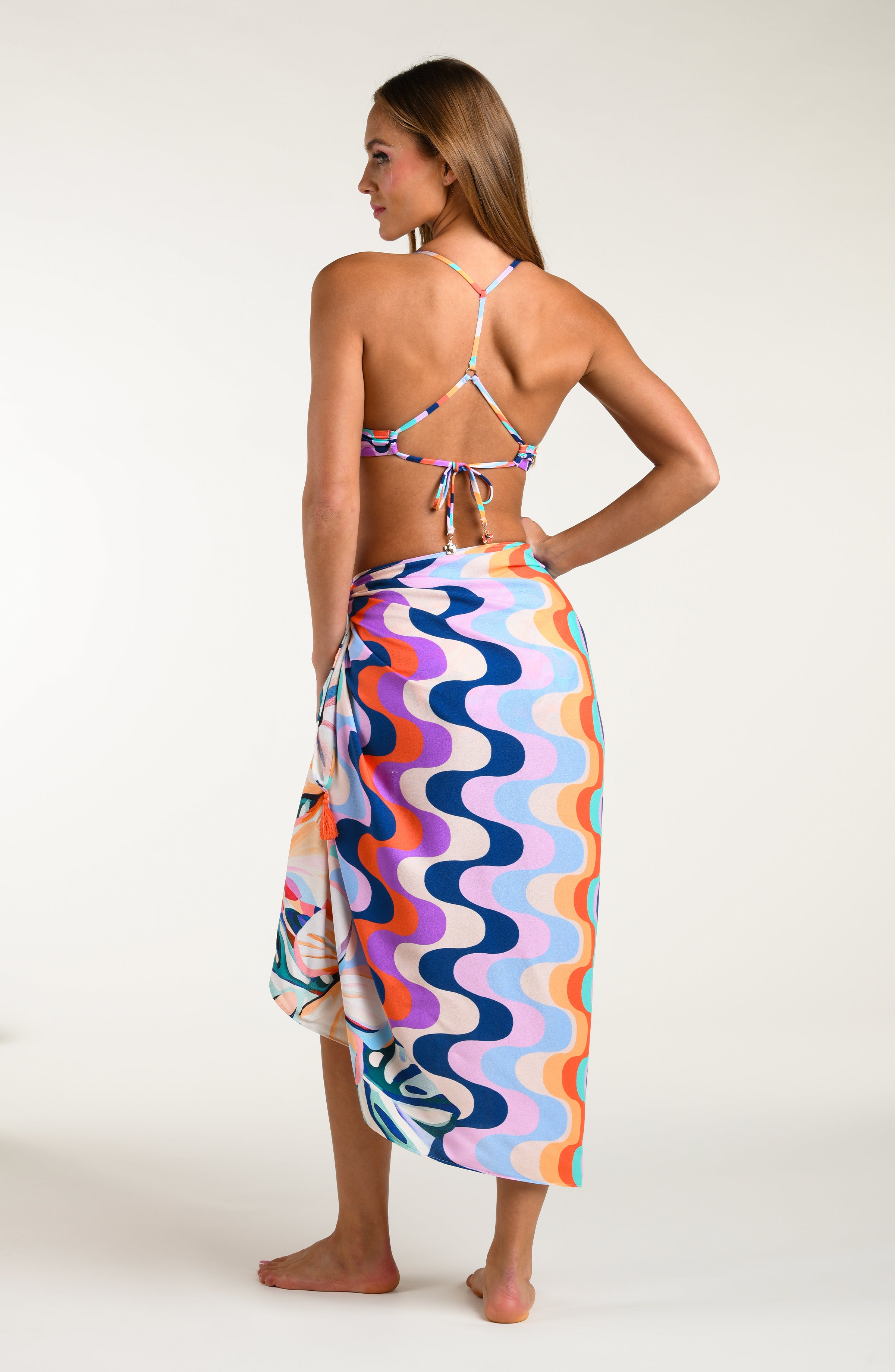 Woman wearing a multicolored patterned bikini top and matching pareo wrap on a white background