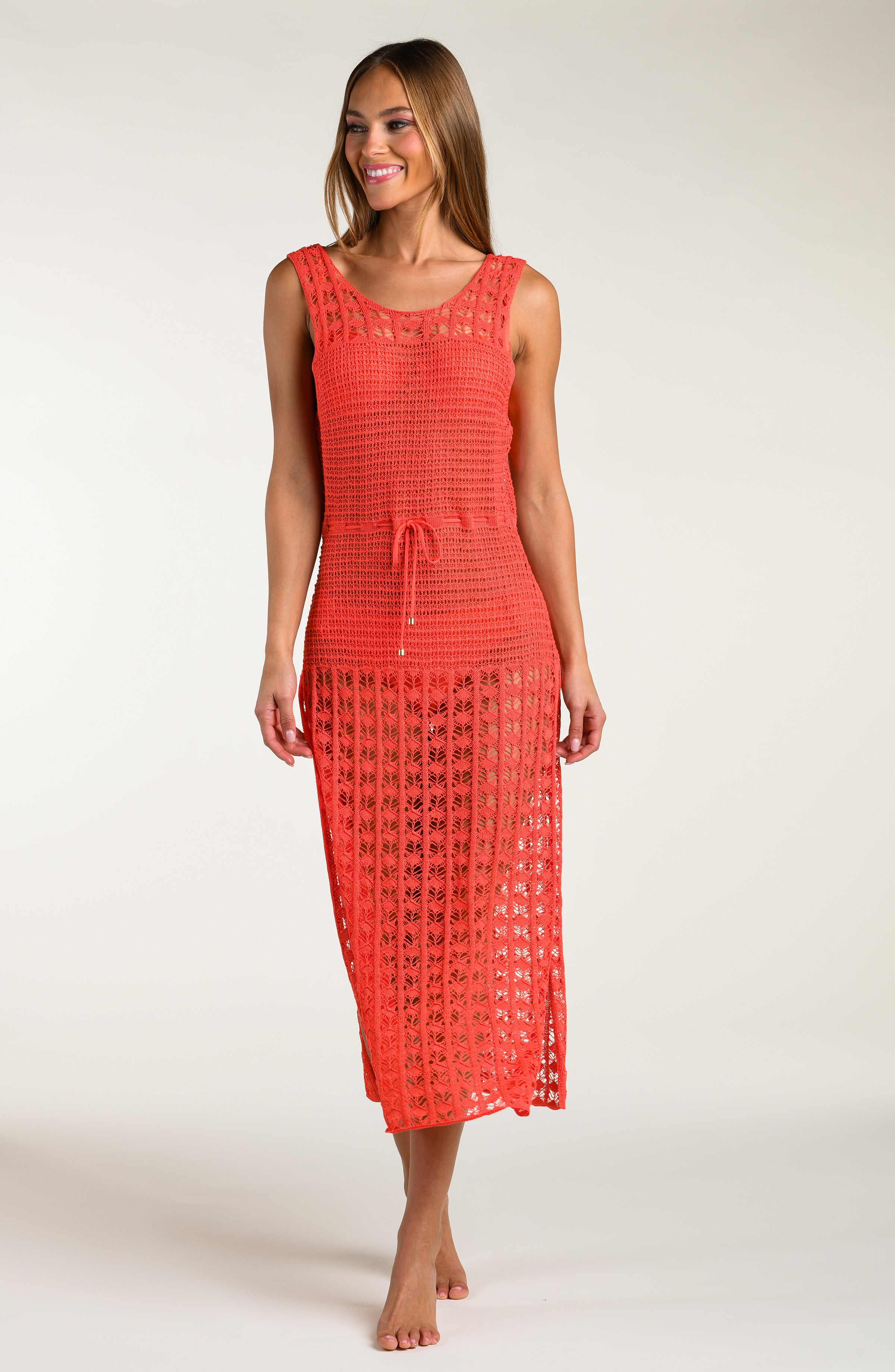 Woman wearing a bright orange maxi dress with a white lace overlay on a white background