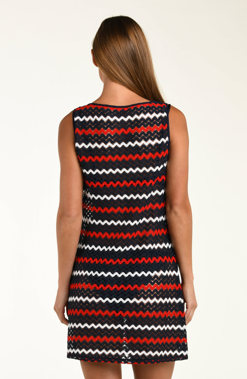 Woman wearing a sleeveless dress with a red, black, and white zigzag pattern on a plain background