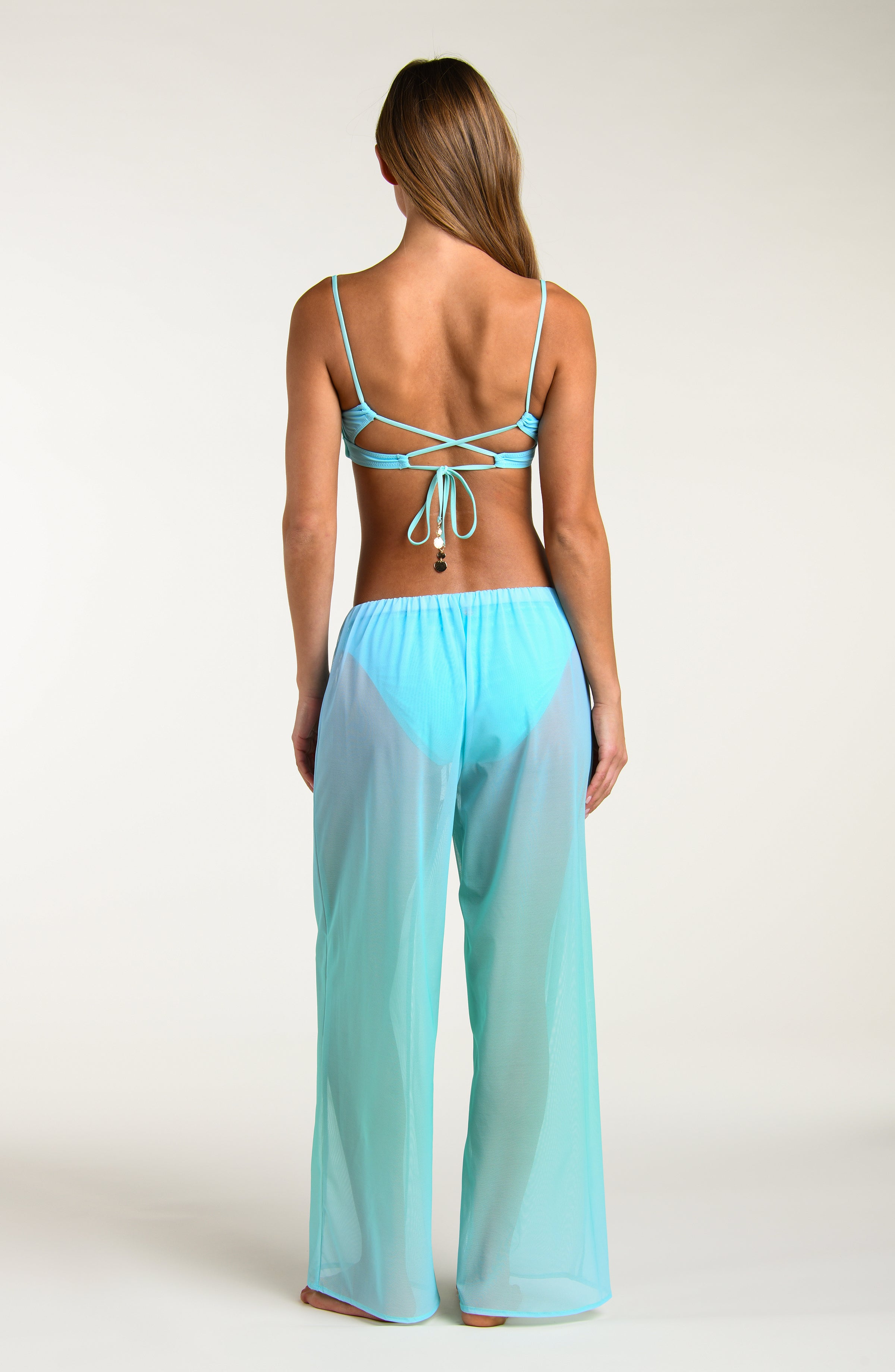 Woman wearing a turquoise colored bikini top and matching sheer pants worn by a person against a white background