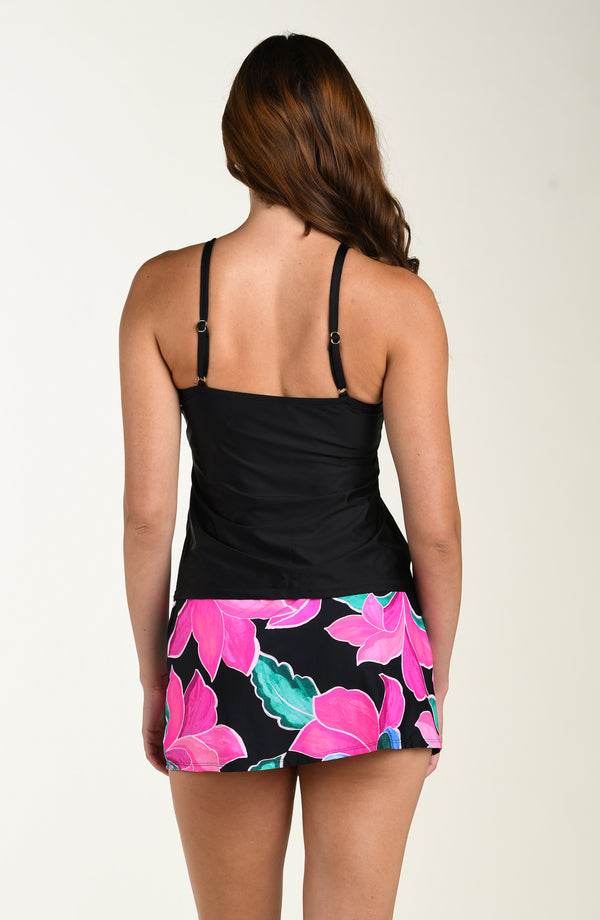 Back image of model wearing a bright multicolored (mostly pink) tropical printed swim skort featuring twist front detail and full rear coverage.