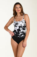 Front image of model wearing a multicolored black and white tropical printed tankini top featuring over the shoulder adjustable straps, removable cups, and side ruching. This is paired with solid black bottoms.