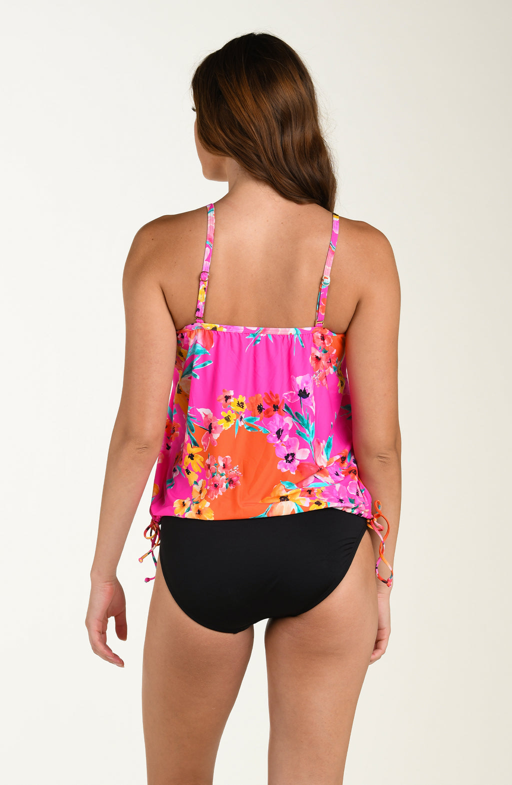 Back image of model wearing a multicolored pink floral printed tankini top featuring a relaxed, flowy fit with adjustable straps, straight back, and a drawstring hem for customizable style. This is paired with solid black colored bikini bottoms.
