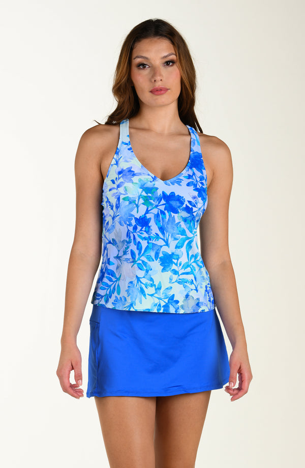 Woman wearing a blue floral tankini and periwinkle skirt on a beige background