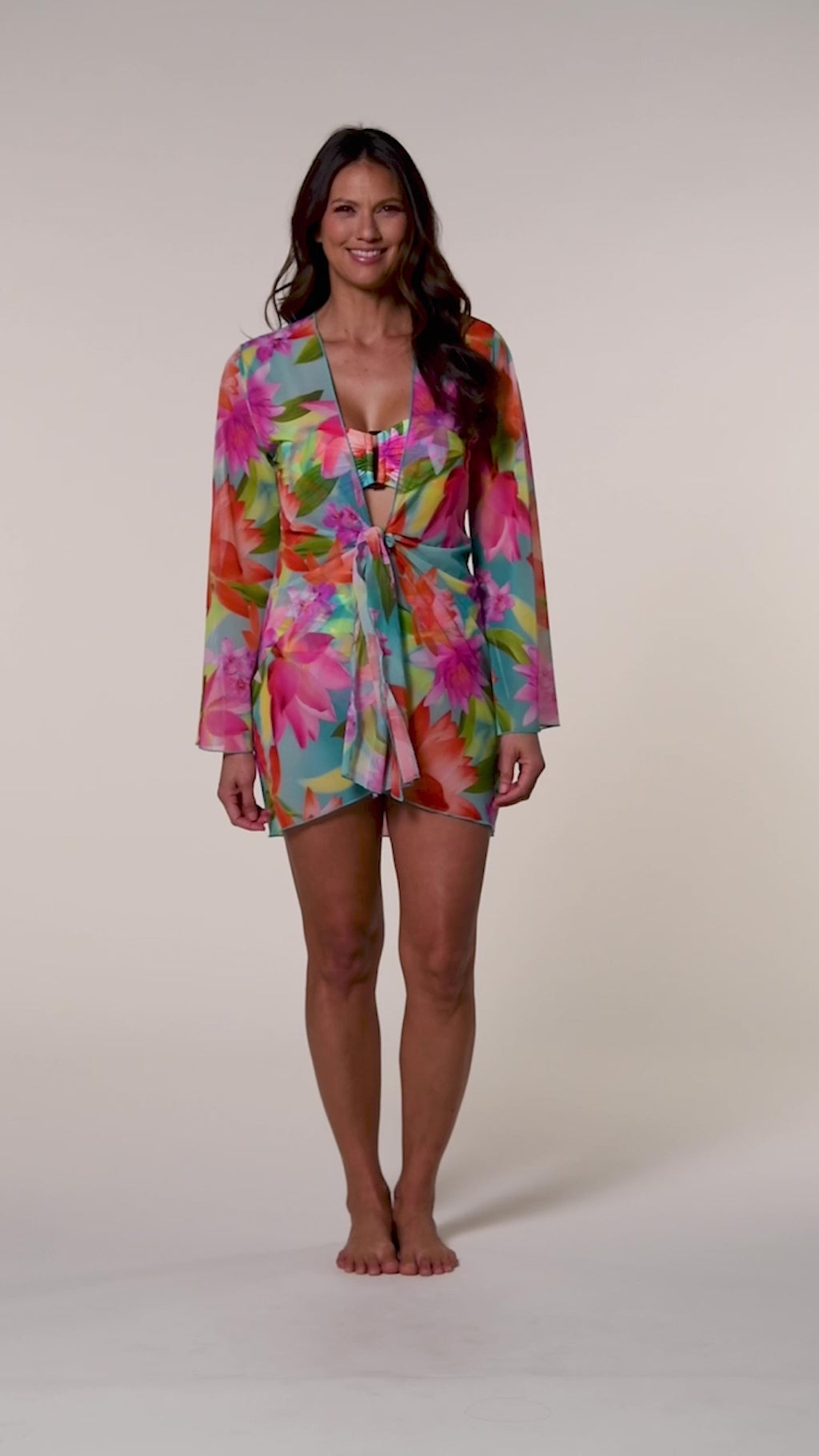 Video of a woman wearing a bright floral kimono cover up with a matching bikini underneath, against a white background.