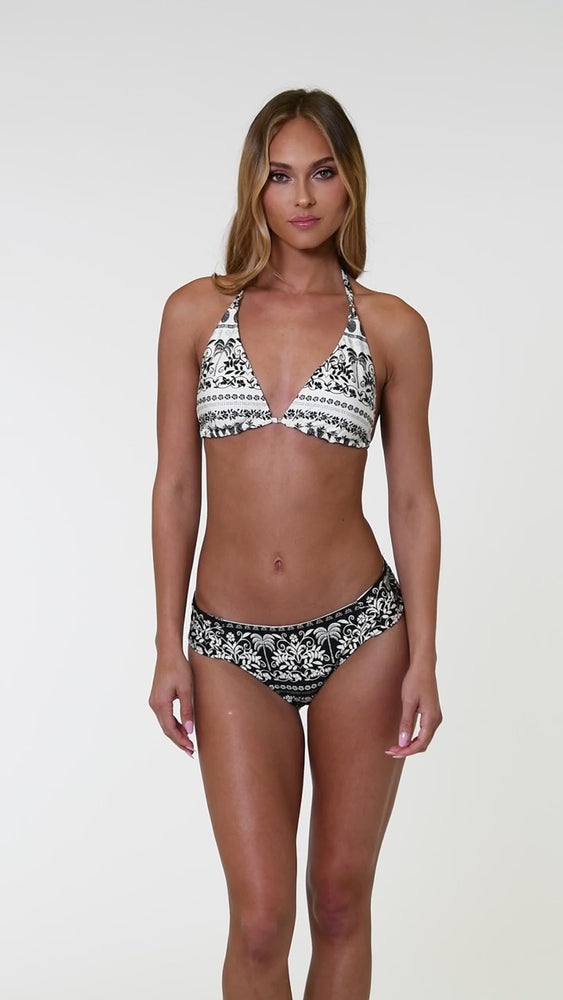 
                  
                    Load and play video in Gallery viewer, Model is wearing a white and black monochromatic patterned side shirred hipster bottom that features an allover tropical motif with hints of palm trees and pineapples set against a black background.
                  
                