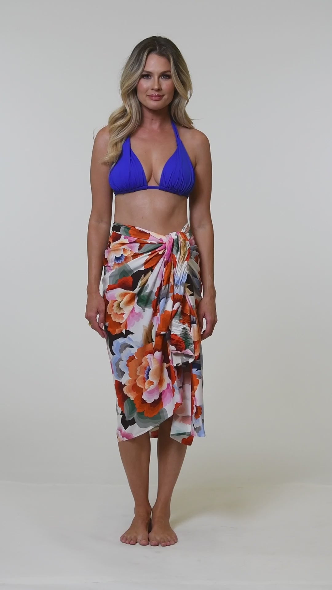 Video of a woman wearing a blue bikini set and a multicolored floral printed pareo cover up. 