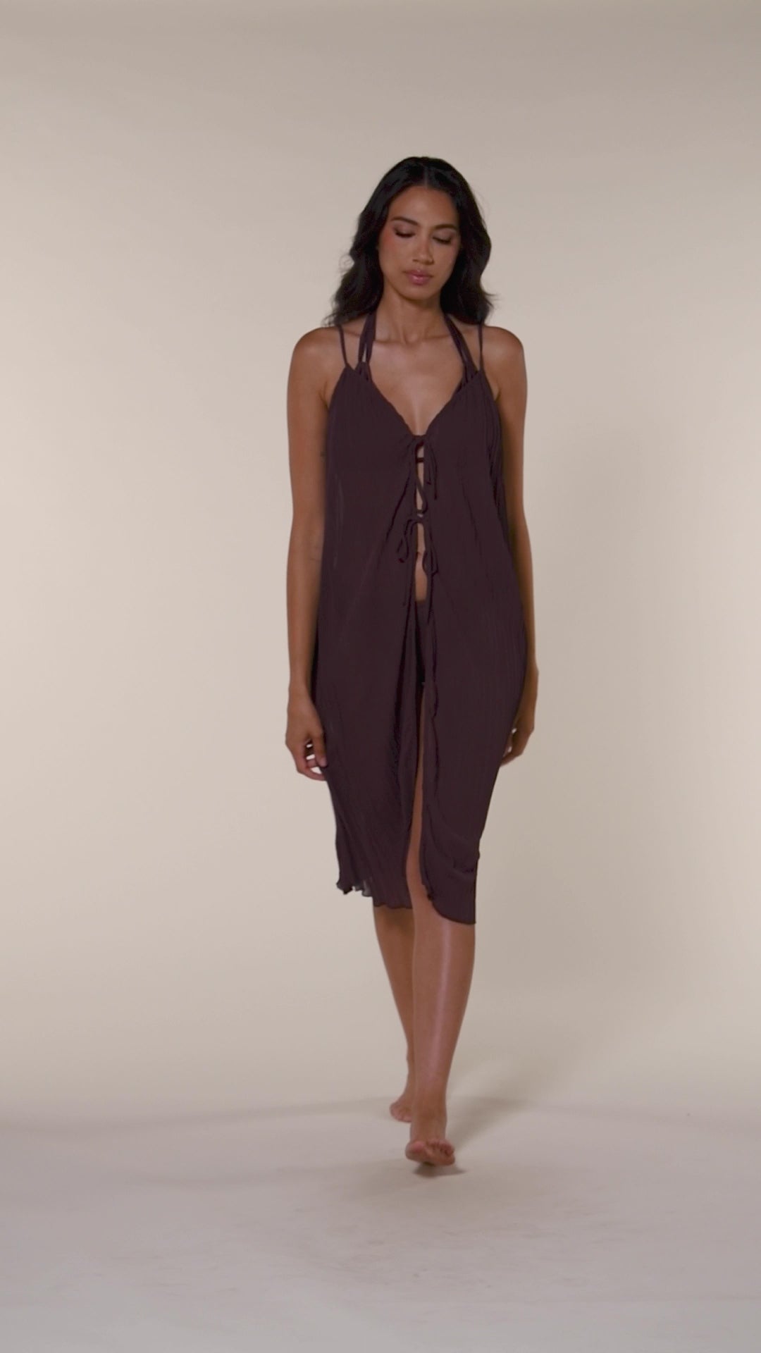 Video of woman wearing a brown dress against an off white background. 
