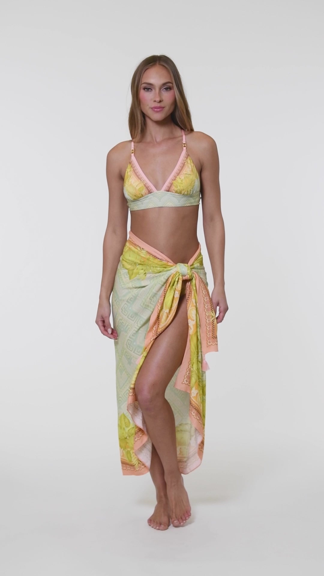 Video of model wearing a multi-colored pastel yellow, green, and peach patterned banded triangle bikini swimsuit top with matching pareo cover up. 