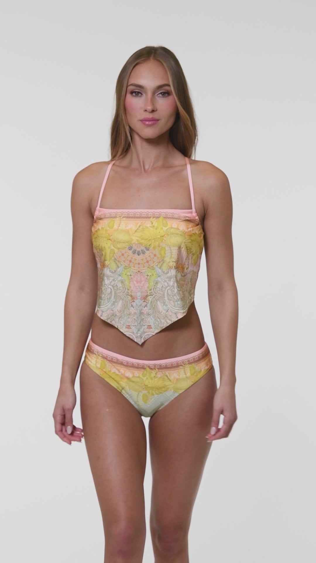 Video of model wearing a multi-colored pastel yellow, green, and peach patterned over the shoulder midkini swimsuit top.