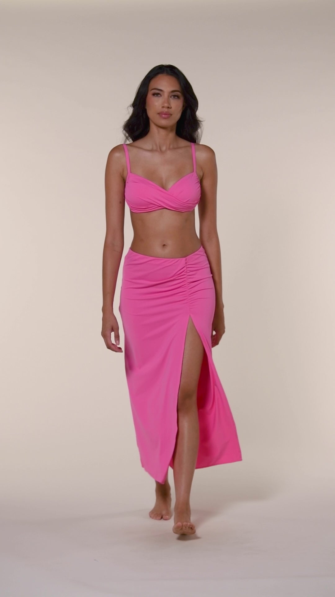 Video of model wearing a rose pink colored bikini top with adjustable thin straps and a wrap-style front. Paired with a rose pink midi skirt.