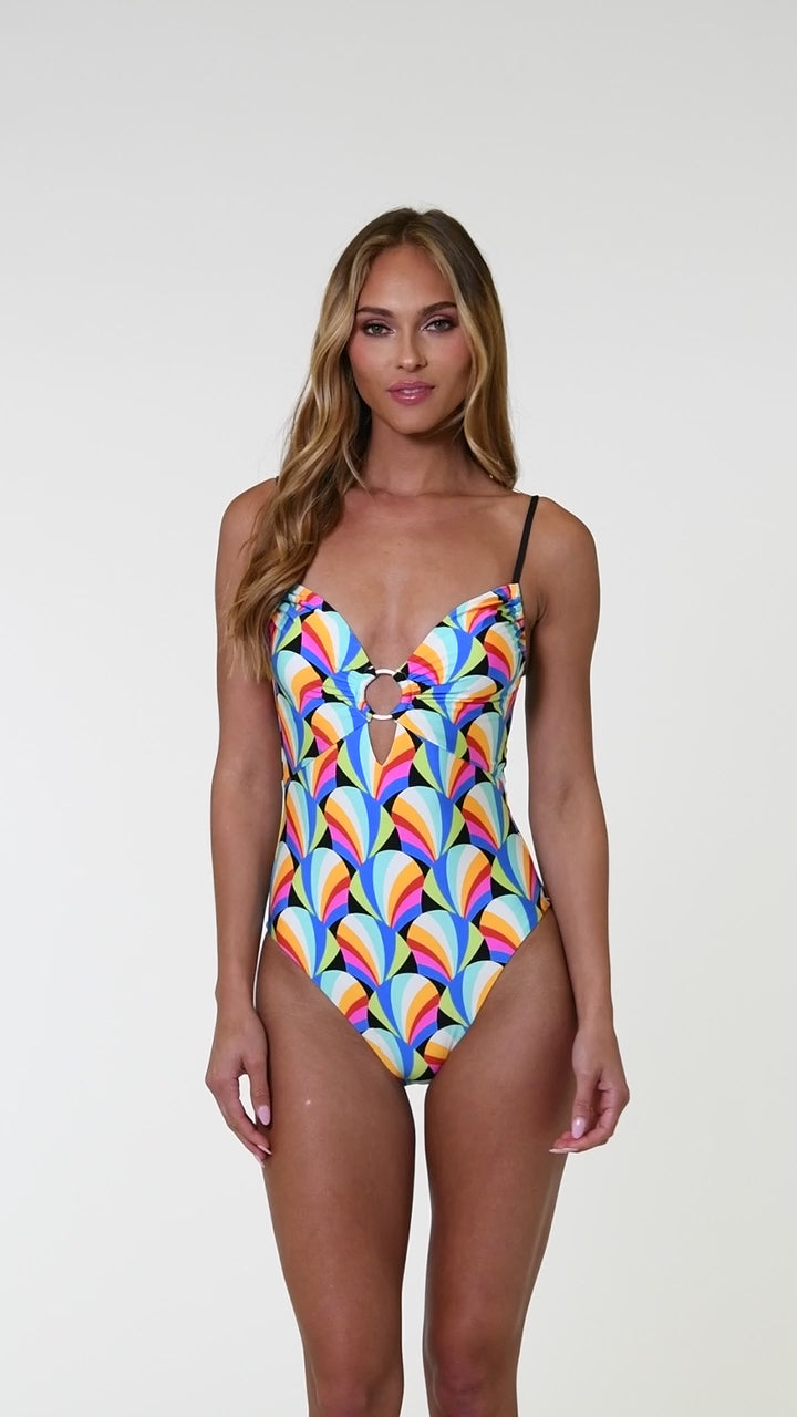 Model is wearing a pink, blue, yellow, and orange multicolored over the shoulder triangle bikini top on a geometric patterned black background.