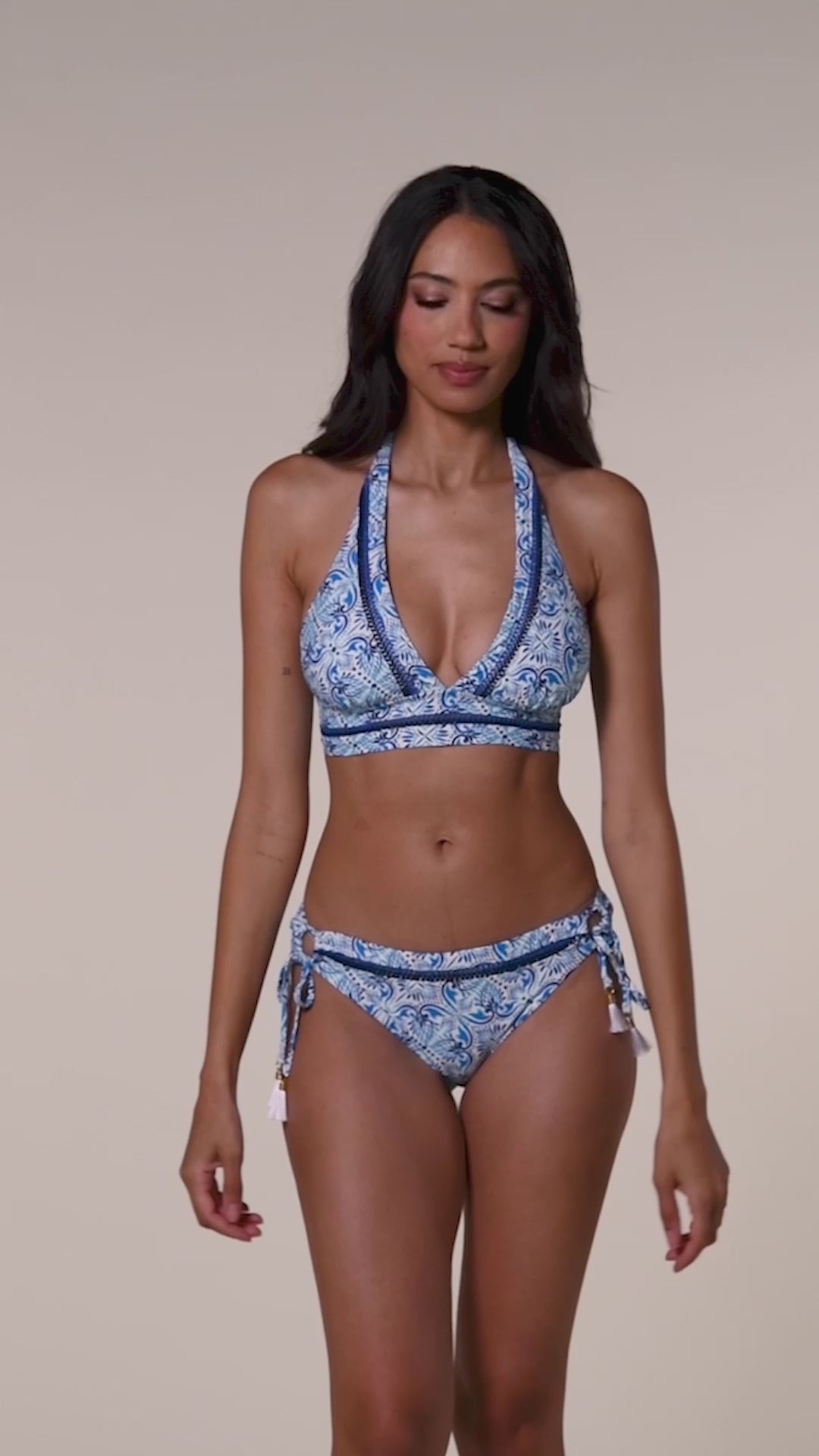 Video of a woman wearing a blue patterned bikini top and matching bottom against a white background.
