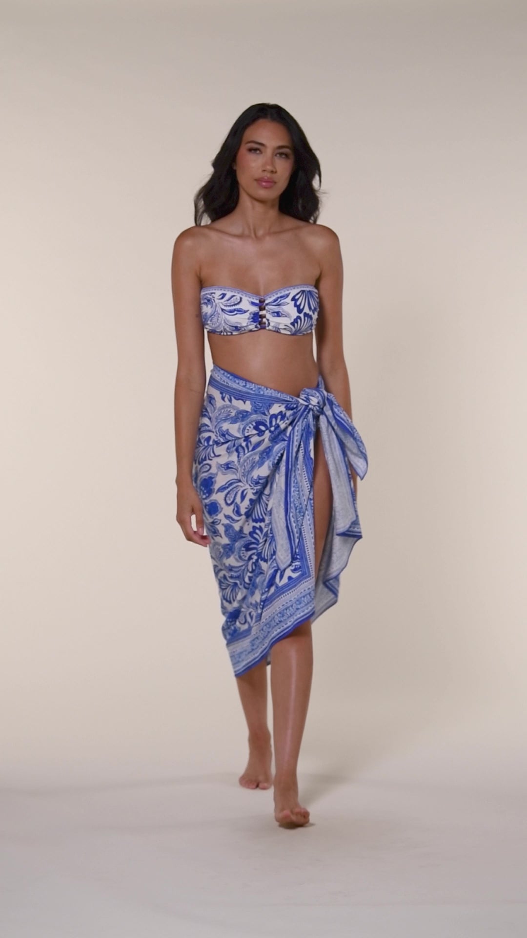Video of woman wearing a blue floral patterned bikini top and matching sarong on a white background