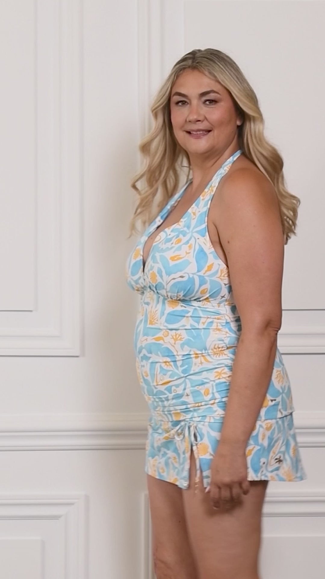 Video of a woman wearing a multicolored blue and white swim skirt against a white background. 