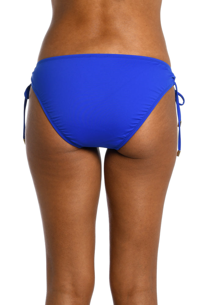 
            
                Load image into Gallery viewer, Model is wearing a sapphire colored side-tie hipster swimsuit bottom from our Best-Selling Island Goddess collection.
            
        