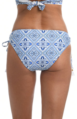 
            
                Load image into Gallery viewer, Model is wearing a light blue artful mosaic printed side-tie hipster swimsuit bottom from our Mediterranean Breeze collection.
            
        
