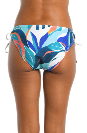 
            
                Load image into Gallery viewer, Model is wearing a blue multi colored tropical printed side tie hipster bottom from our Coastal Palms collection!
            
        