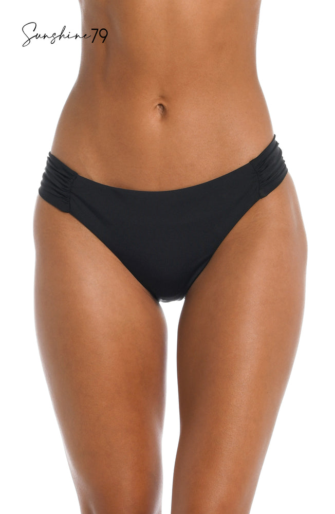 
            
                Load image into Gallery viewer, Model is wearing a solid black side shirred hipster bottom from our Sunshine 79 brand.
            
        