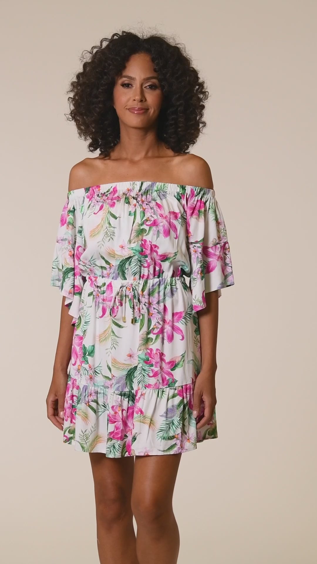 This is a video of a Model is wearing multi colored tropical print on a white backround with this off shoulder cover up dress from our Mystic Palms collection!